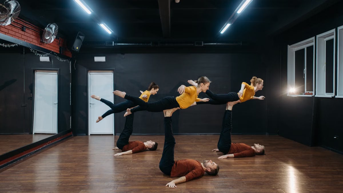 Five dancers showcase flexibility and balance in a dance studio during rehearsal.